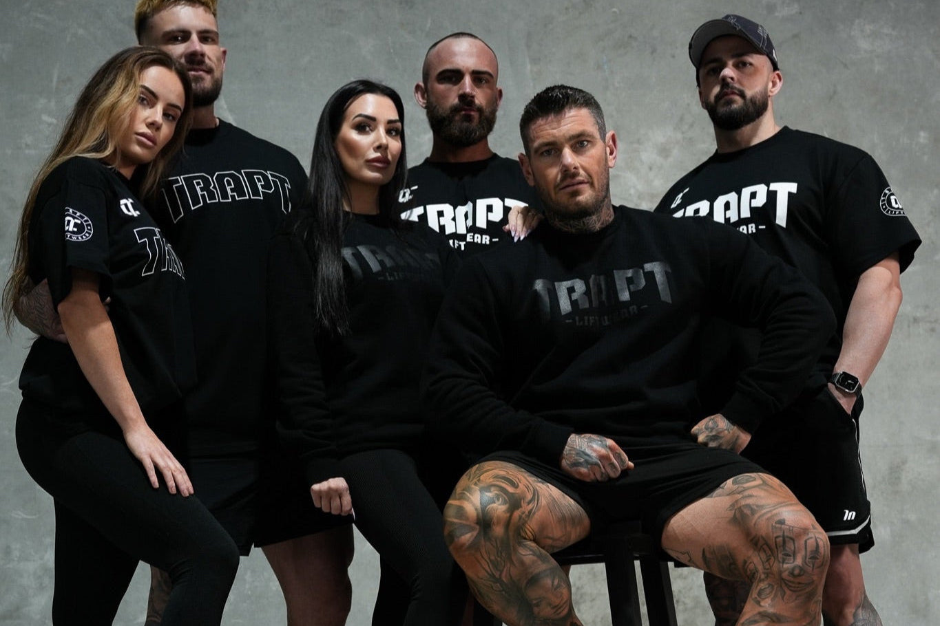 Group of people wearing black 'TRAPT' t-shirts against a gray background